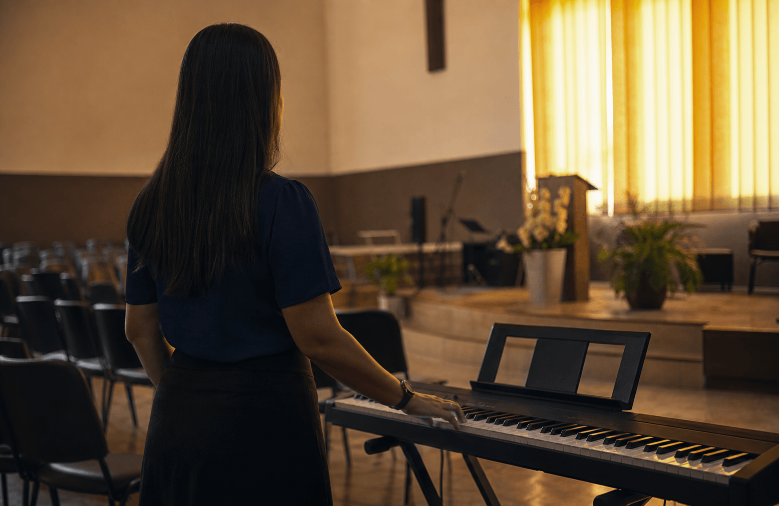 Teclado disponível em uma igreja simples antes do culto, com uma pessoa ainda insegura para tocar