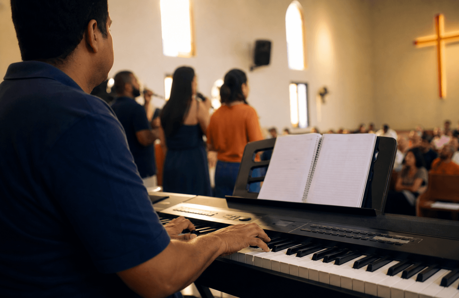 Tecladista acompanhando um ensaio simples na igreja com pessoas cantando ao fundo